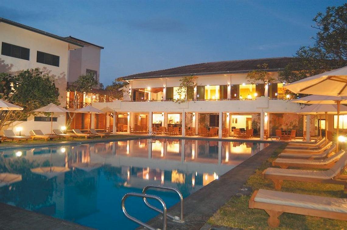 Außenbereich des Mermaid Hotel & Club bei Nacht mit Swimmingpool, Sonnenliegen und Sonnenschirmen.