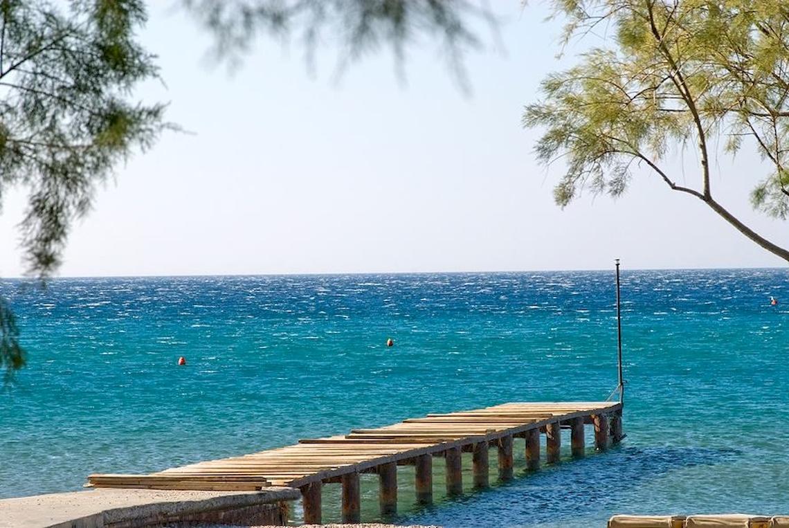 Foto des Doryssa Seaside Resort Piers, der ins Meer ragt, mit blauem Wasser und Bäumen im Hintergrund.