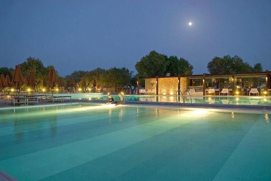 Nachtansicht des Swimmingpools des Doryssa Seaside Resort mit beleuchteten Sonnenschirmen und Sitzgelegenheiten.