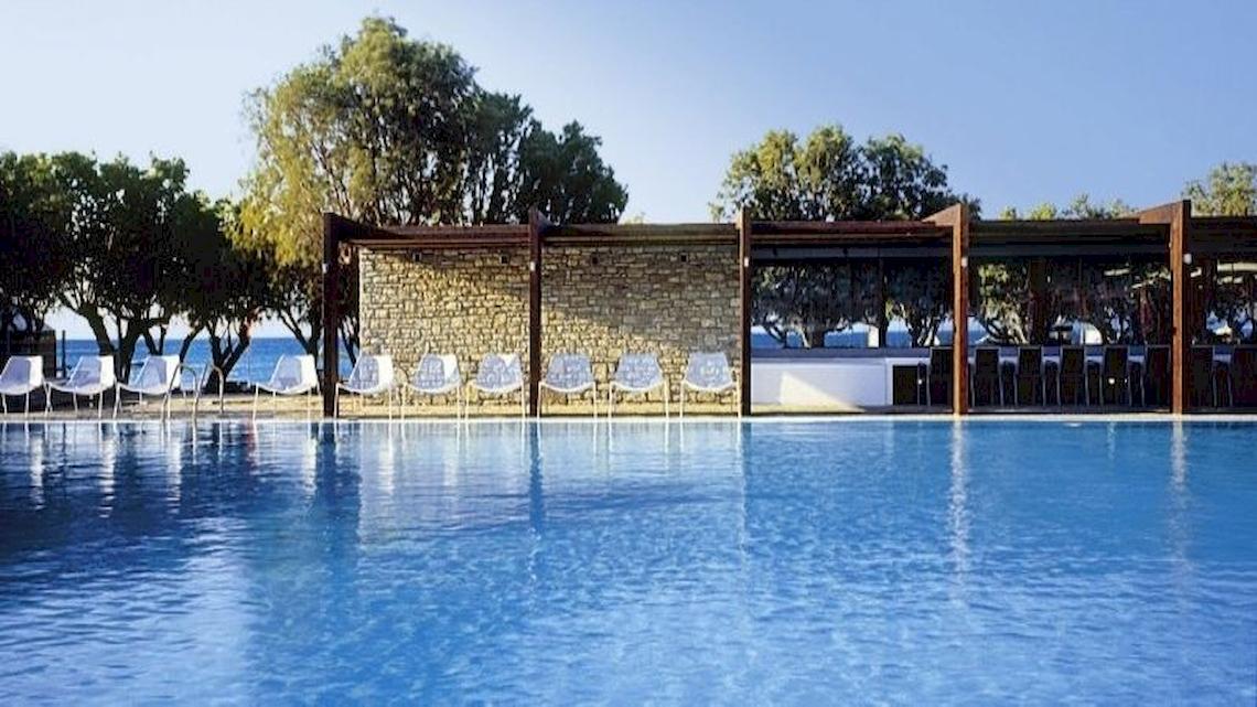 Pool-Bereich des Doryssa Seaside Resorts mit weißen Stühlen und Tischen am Meer