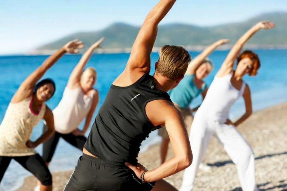 Gruppe von Frauen und Männern, die Yoga am Strand des Doryssa Seaside Resort machen