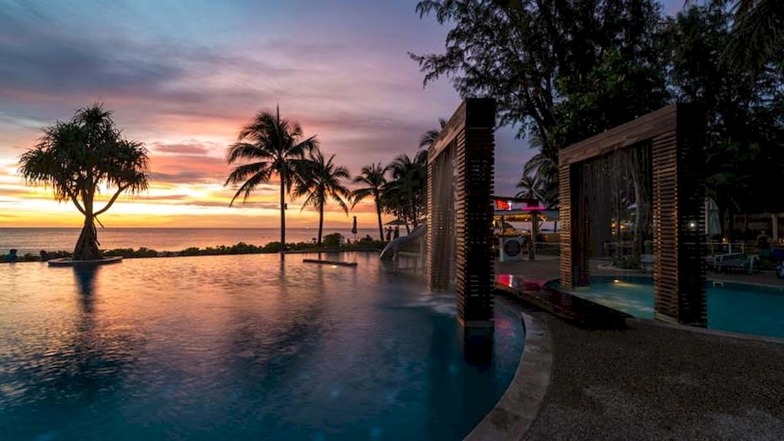 Katathani Phuket Beach Resort Pool bei Sonnenuntergang mit Blick auf den Ozean und Palmen.