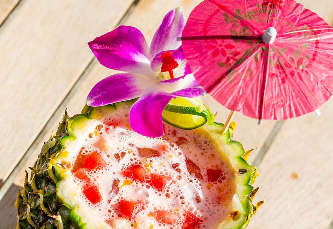 Cocktail in einer Ananasschale mit einem roten Schirm und einer Blume
