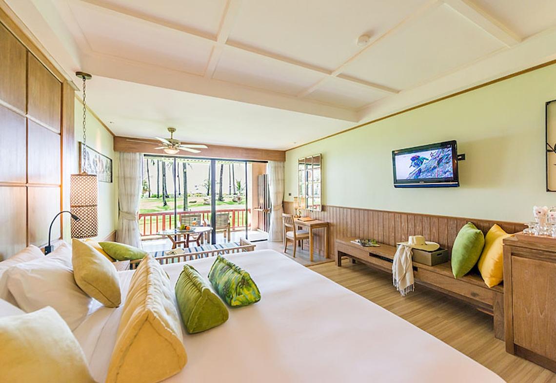 Innenansicht einer Suite im Katathani Phuket Beach Resort mit einem großen Bett, grünen Kissen und einem Fernseher an der Wand.