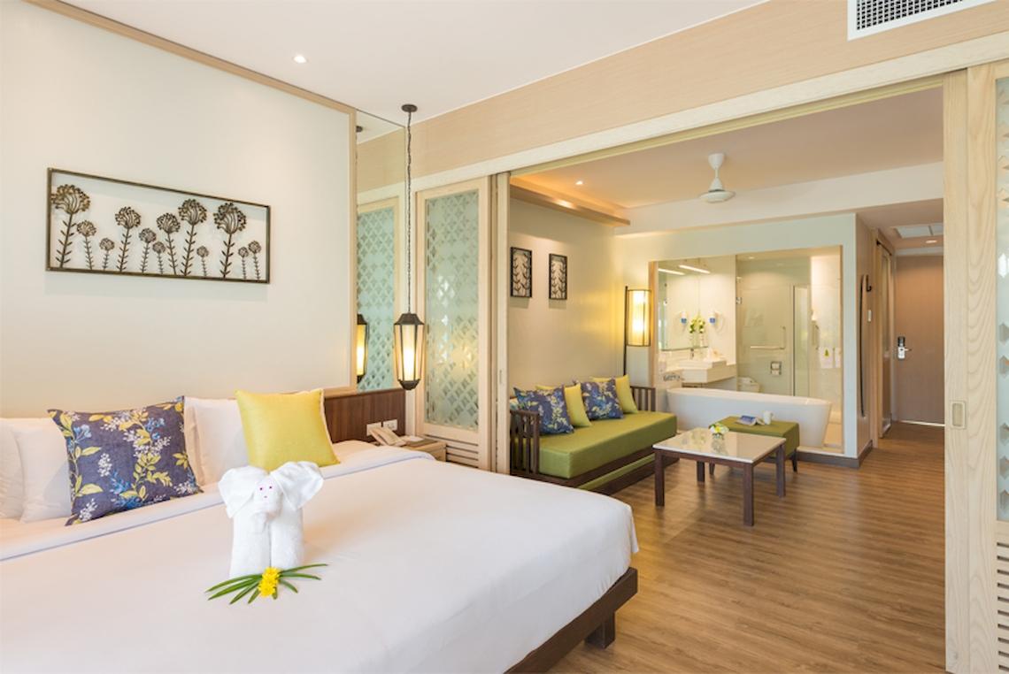 Innenansicht eines Hotelzimmers im Katathani Phuket Beach Resort mit Bett, Sofa und Badewanne.