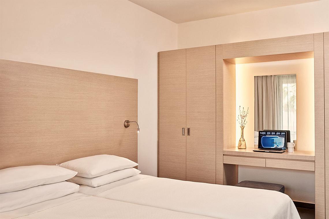 Schlafzimmer im Atlantica Mikri Poli Kos Hotel mit zwei Betten, einem Laptop auf dem Schreibtisch und einer Lampe.