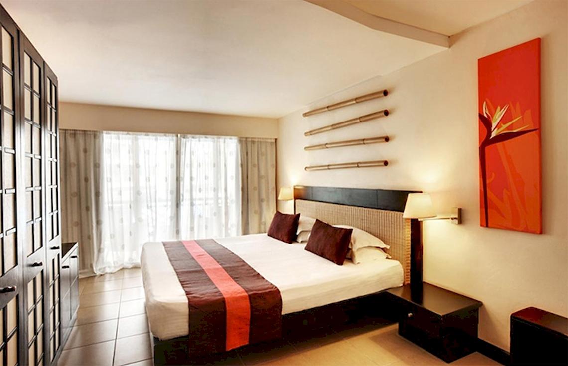 Doppelbett im Schlafzimmer im Pearle Beach Resort & Spa mit braunen Kissen und weißer Bettwäsche.