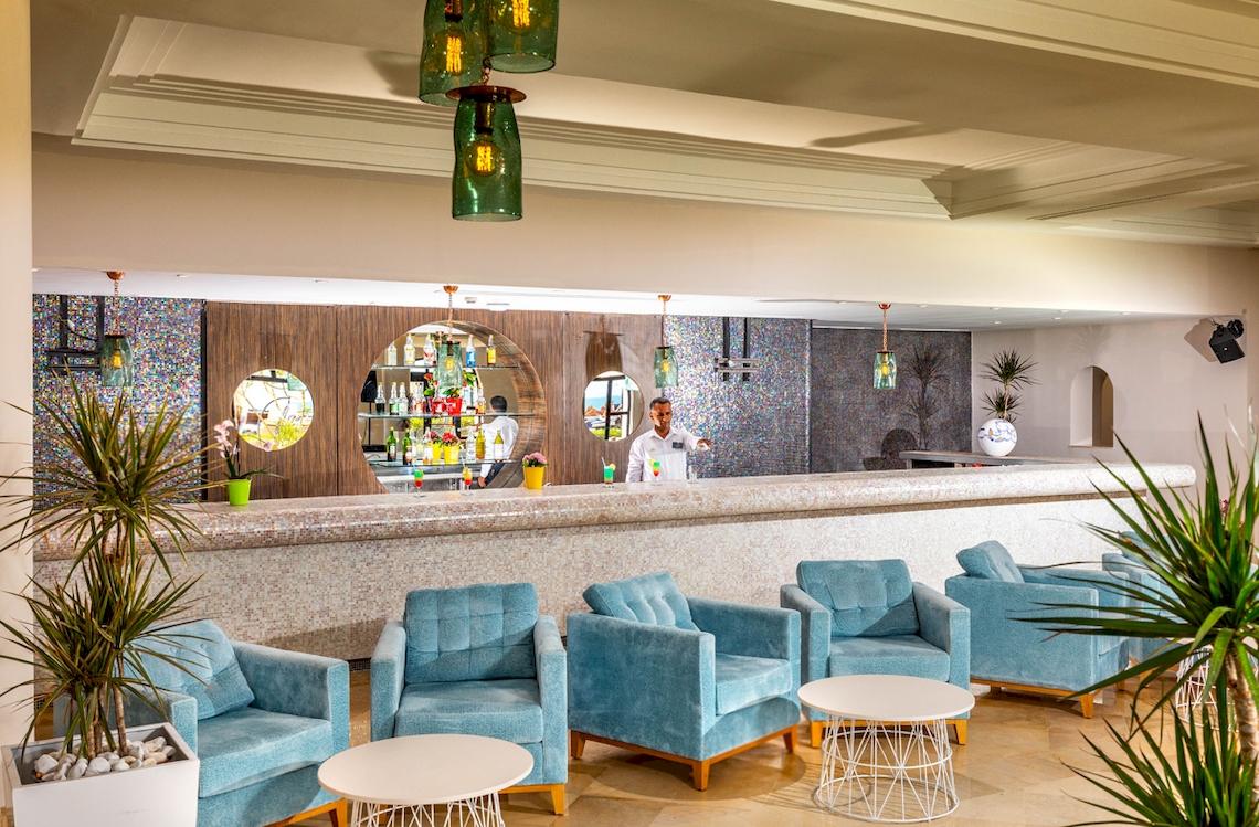 Innenansicht der Bar im Ulysse Djerba Thalasso & Spa Hotel mit Barkeeper und blauen Sesseln.