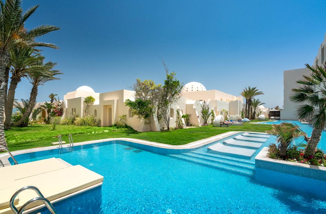 Außenpool des Ulysse Djerba Thalasso & Spa Hotels mit weißen Gebäuden und palmengesäumten Rasen.