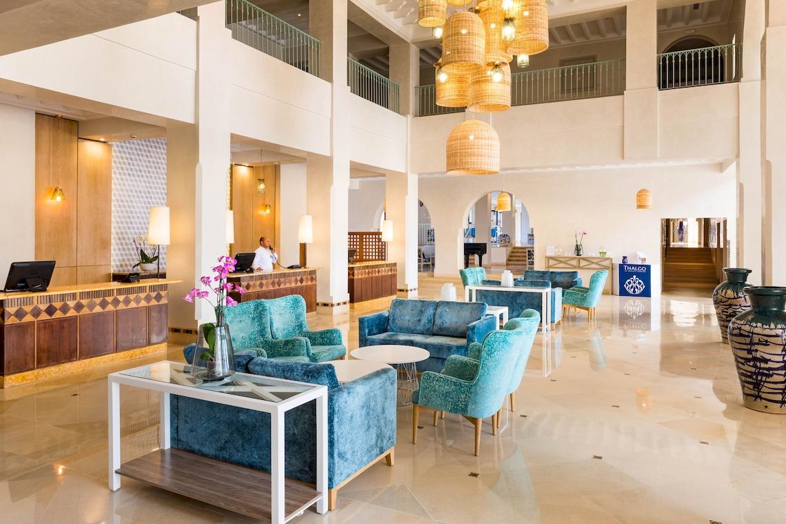 Lobby des Ulysse Djerba Thalasso & Spa Hotels mit blauen Sofas, weißen Tischen und hängenden Lampen.