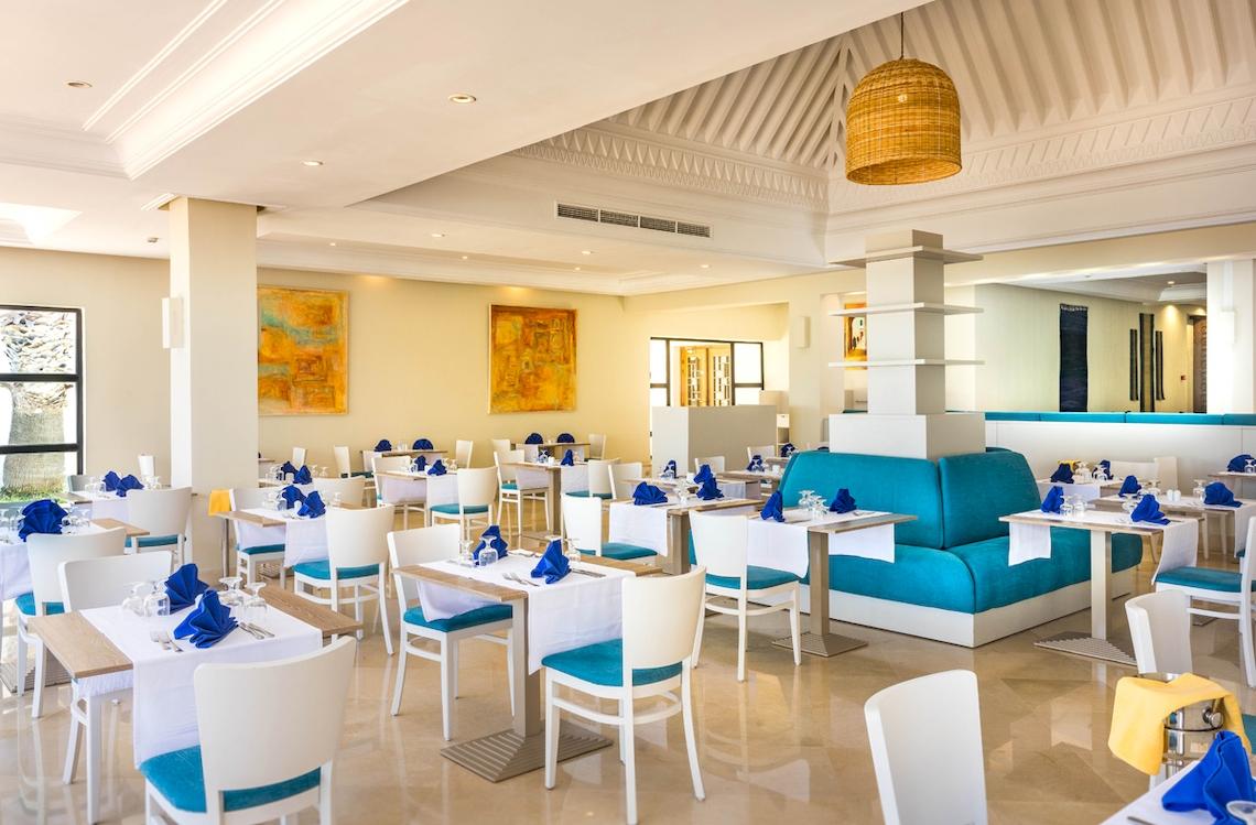 Innenansicht des Restaurants im Ulysse Djerba Thalasso & Spa Hotel mit blauen Sofas und weißen Tischen.