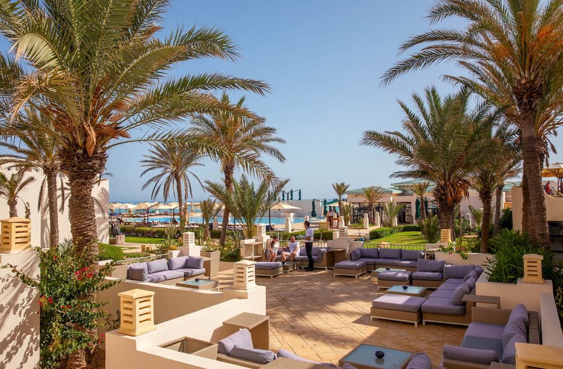 Außenterrasse des Ulysse Djerba Thalasso & Spa Hotels mit Palmen, Loungemöbeln und Blick auf das Meer.