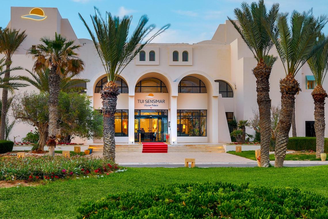 Außenansicht des Ulysse Djerba Thalasso & Spa Hotels mit gepflegtem Rasen und hohen Palmen vor dem Eingang.
