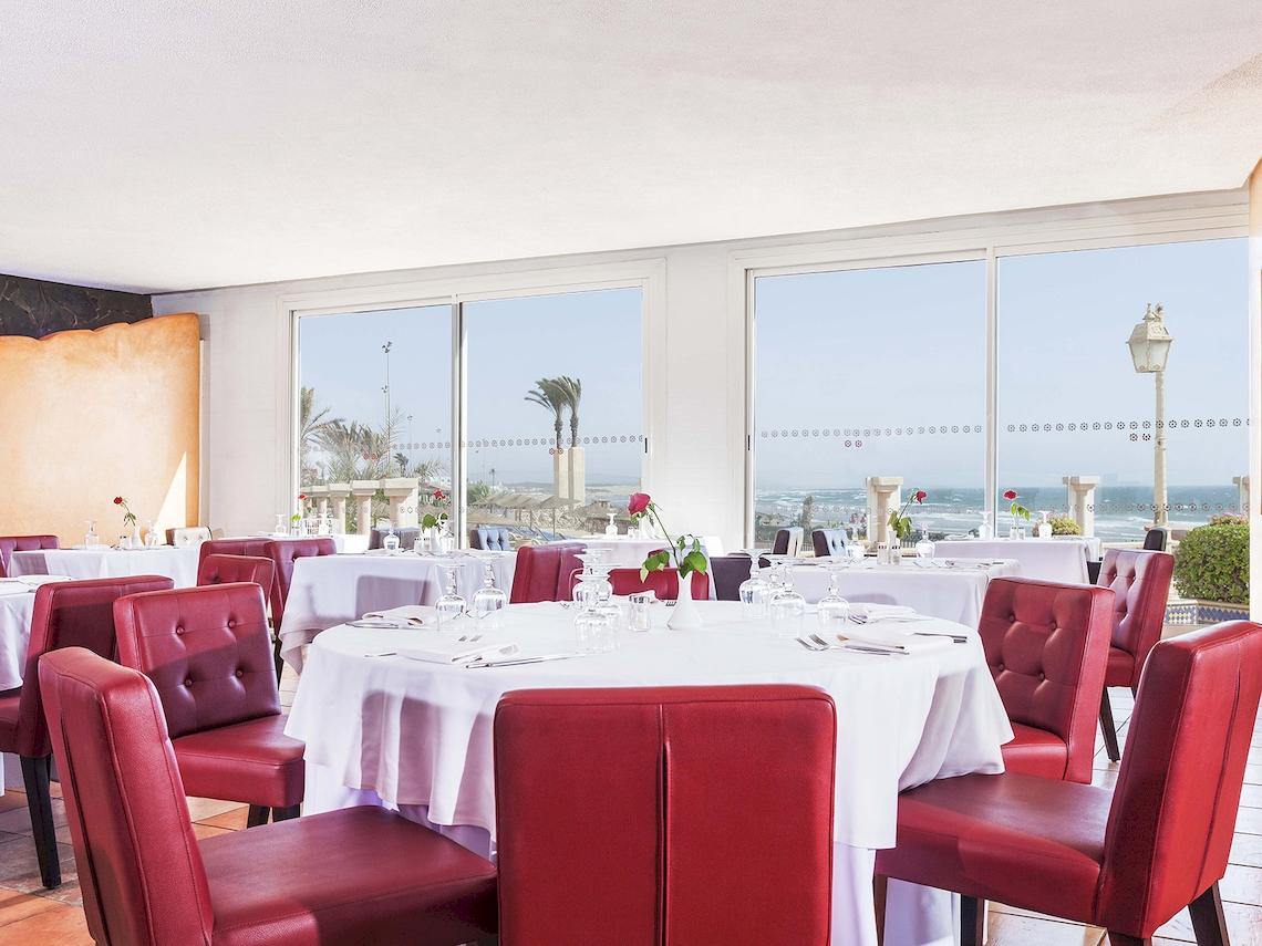 Innenansicht des Restaurants im Atlas Amadil Beach Hotel mit Blick auf das Meer und roten Stühlen.