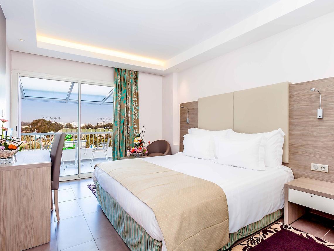 Innenansicht eines Hotelzimmers im Atlas Amadil Beach Hotel mit einem Bett, einem Schreibtisch und einem Balkon