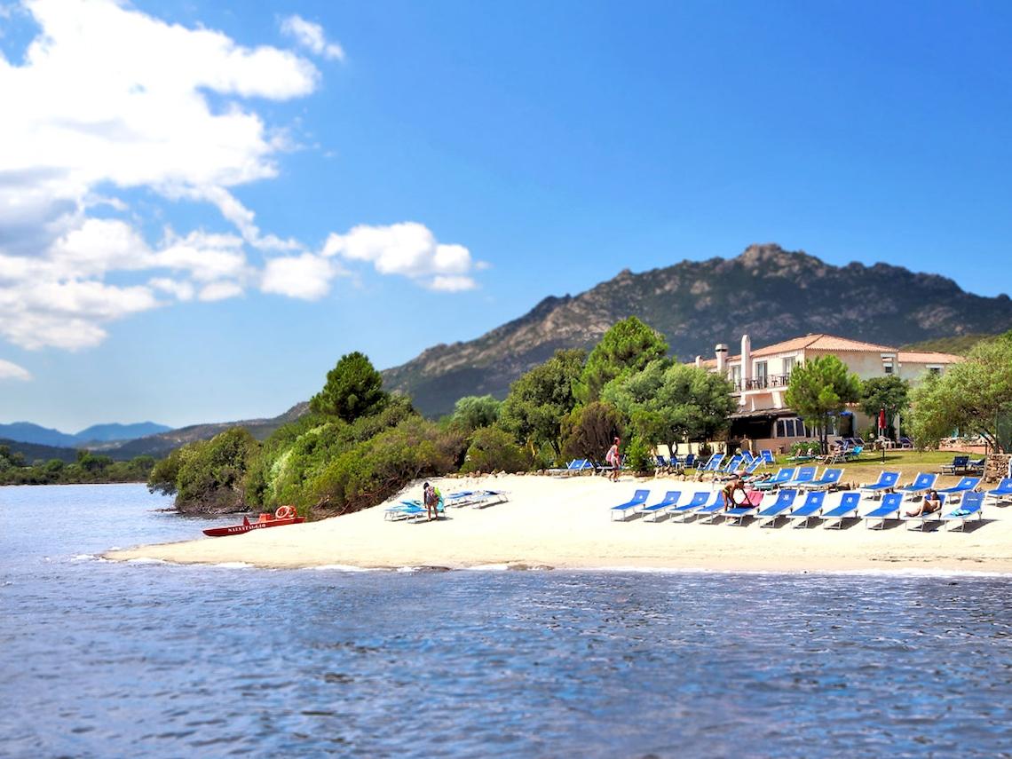 Strand mit blauen Liegestühlen und einem Hotel im Hintergrund.