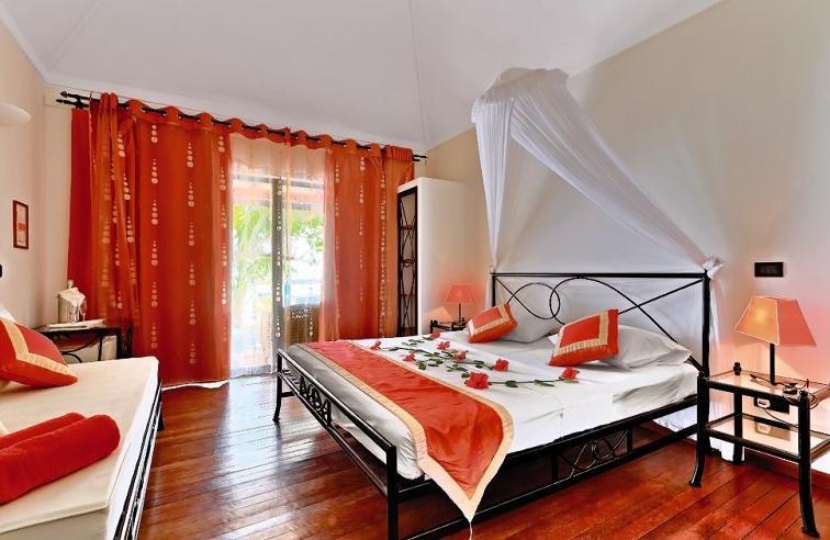 Ein Schlafzimmer im Nakai Maayafushi Resort mit einem Doppelbett und einem Sofa, beide mit roten Kissen und weißen Laken.