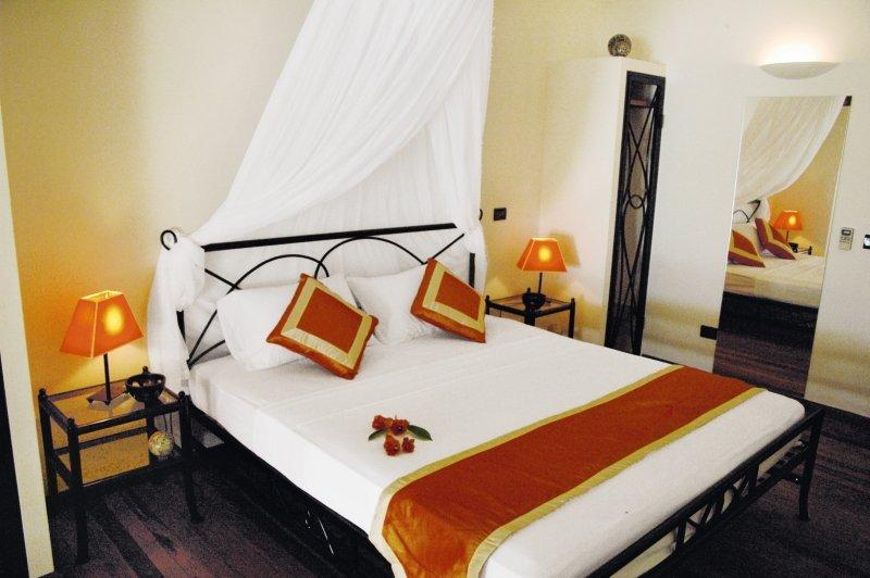 Schlafzimmer im Nakai Maayafushi Resort mit einem Bett, Kissen, Lampen und einem Spiegel.