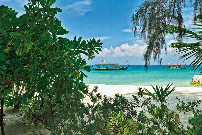 Blick auf den Strand des Nakai Maayafushi Resorts mit zwei Booten im Wasser und üppiger Vegetation.