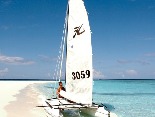 Eine Frau steht neben einem weißen Katamaran mit der Nummer 3059 am Strand