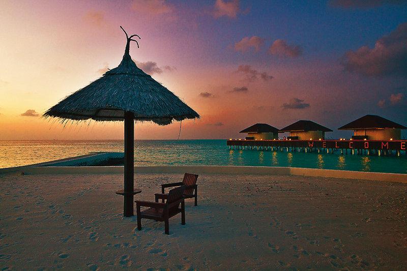 Strand des Nakai Maayafushi Resorts mit Sonnenuntergang, Strandstuhl und Sonnenschirm.