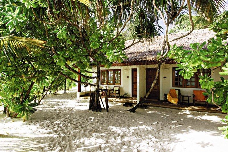 Strandhaus des Nakai Maayafushi Resorts, umgeben von Bäumen und Sand.