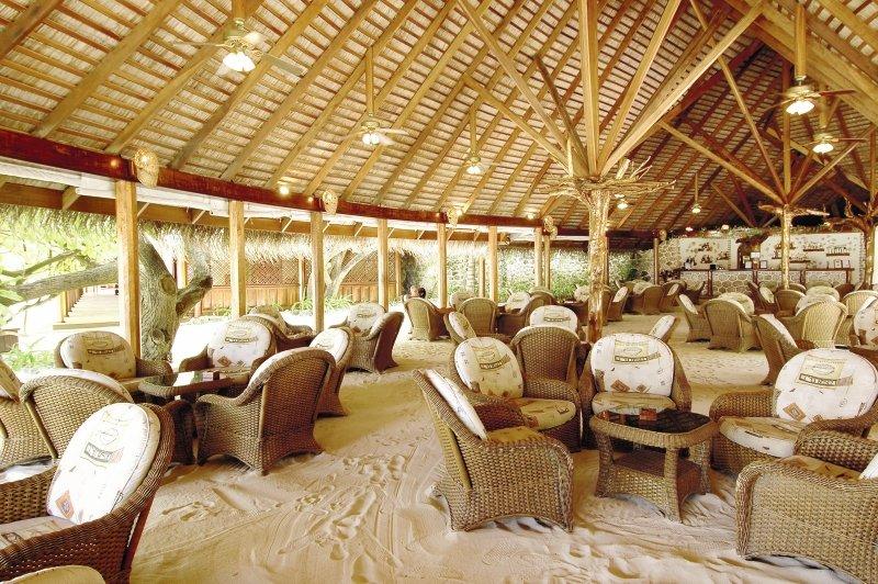 Innenbereich des Nakai Maayafushi Resorts mit vielen Rattan-Stuhlreihen und Tischen auf einem Sandboden.