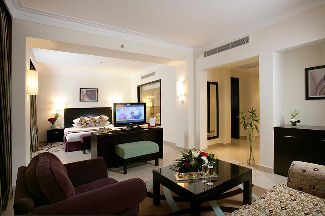 Innenansicht eines Zimmers im Rixos Sharm El Sheikh Hotel mit Bett, Fernseher und Wohnzimmermöbeln.
