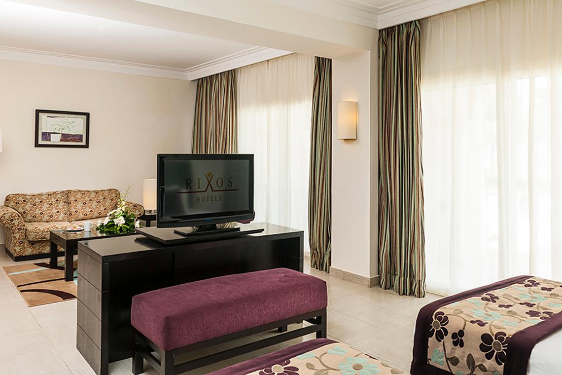 Ein modernes Hotelzimmer im Rixos Sharm El Sheikh mit Fernseher, Sofa, Tisch und zwei Betten.