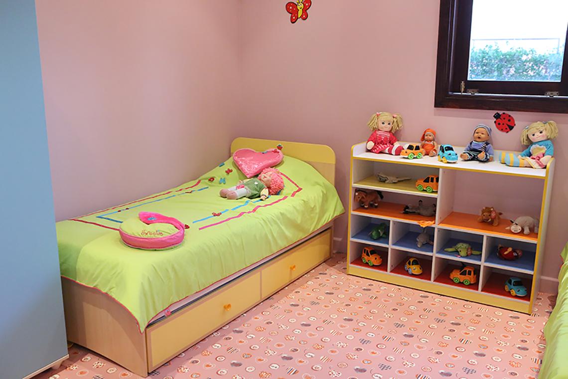 Ein rosa und grün gestrichenes Kinderzimmer mit einem Bett und einem Spielzeugschrank.