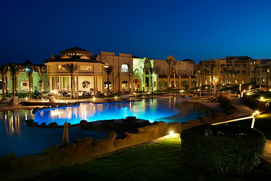 Nachtansicht des Rixos Sharm El Sheikh Hotels mit beleuchtetem Swimmingpool und illuminierten Gebäuden.