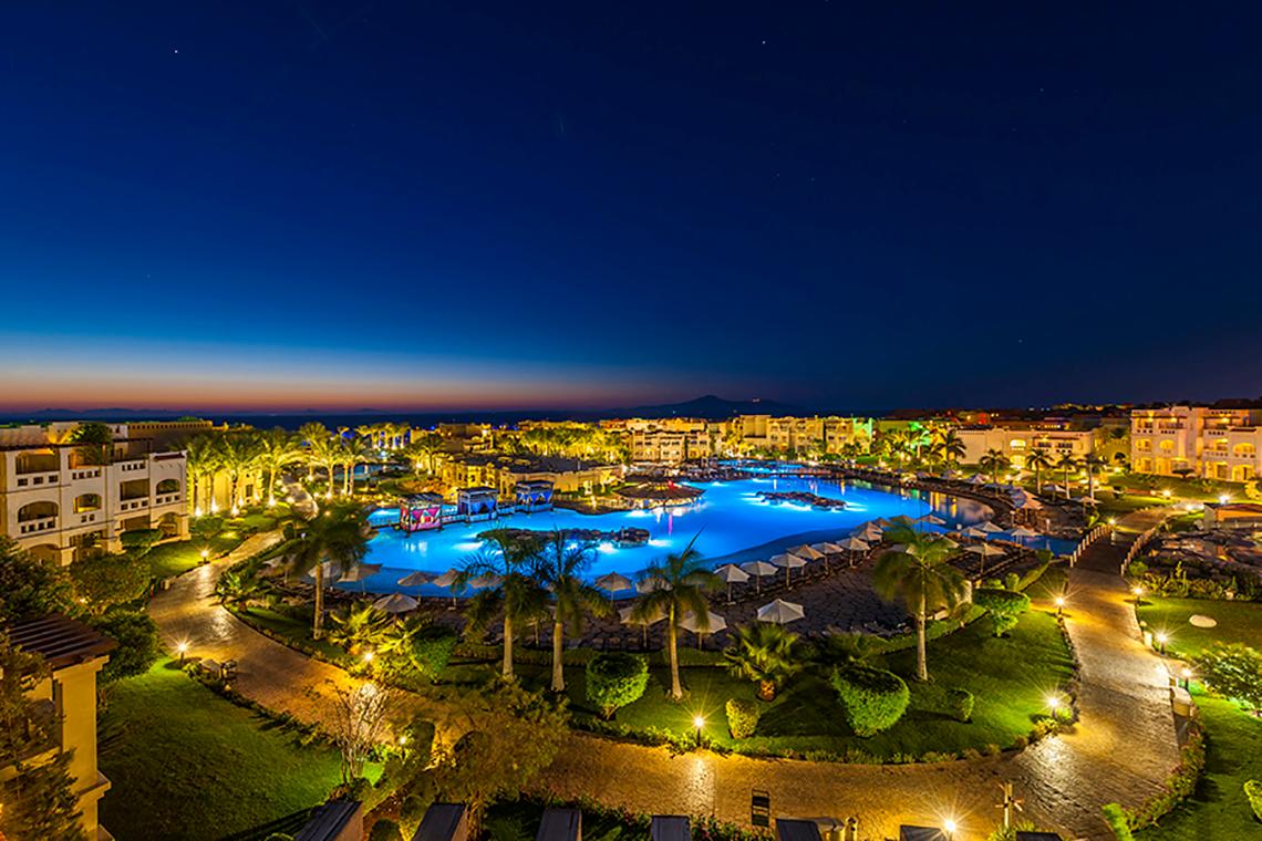 Abendansicht des Rixos Sharm El Sheikh Resorts mit beleuchtetem Swimmingpool und angelegter Landschaft.