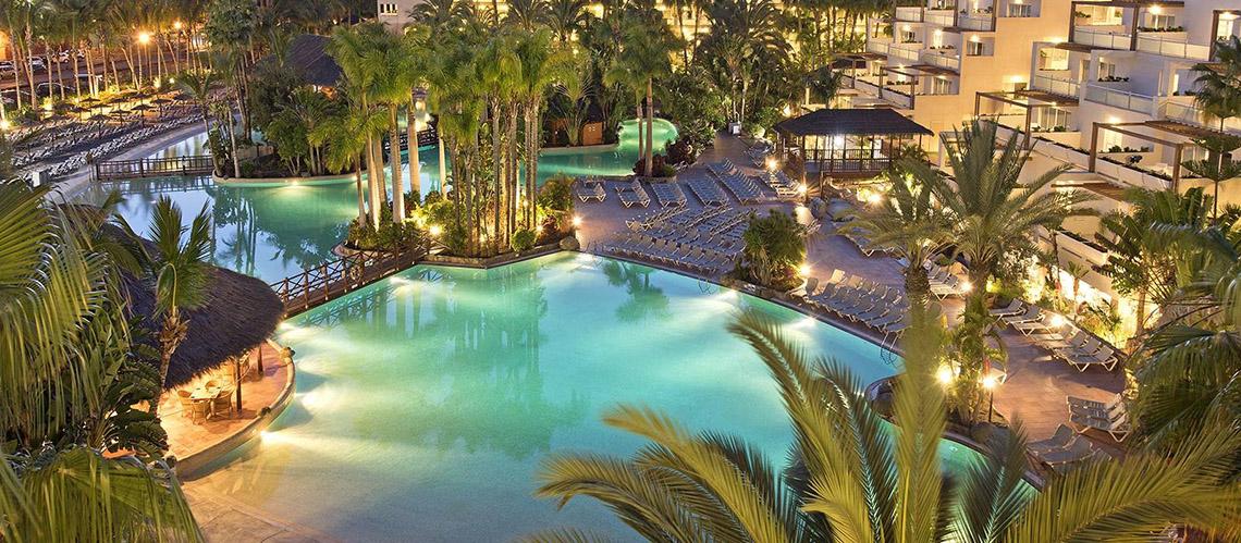 Ein Swimmingpool und eine Lounge im Tabaiba Princess Hotel, umgeben von Palmen und Sonnenliegen.