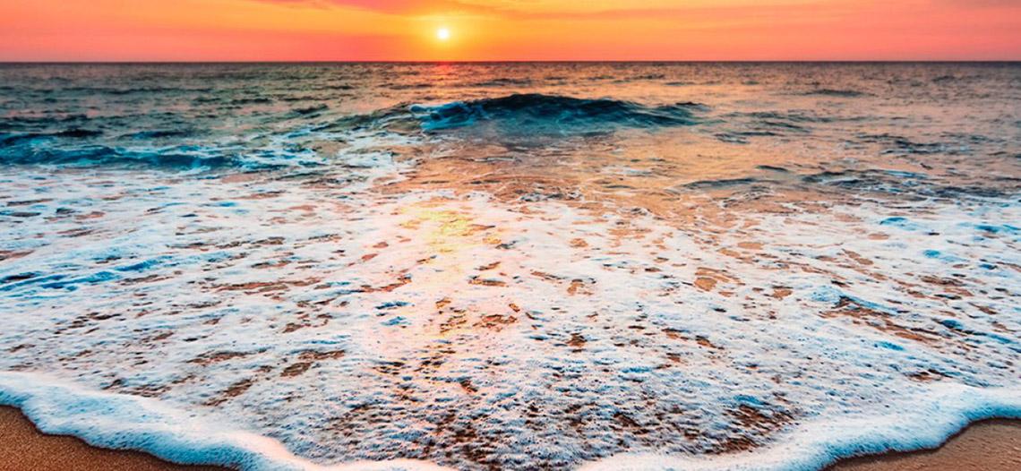 Sonnenuntergang am Meer mit sanften Wellen und einem Hotel namens Tabaiba Princess.