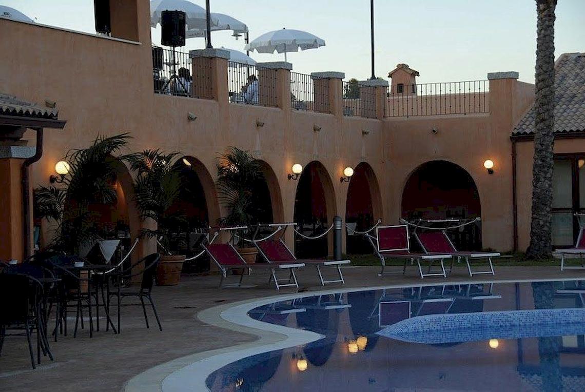 Abendaufnahme des Poolbereichs im Alma Resort mit Lounge-Stühlen und Pflanzen.
