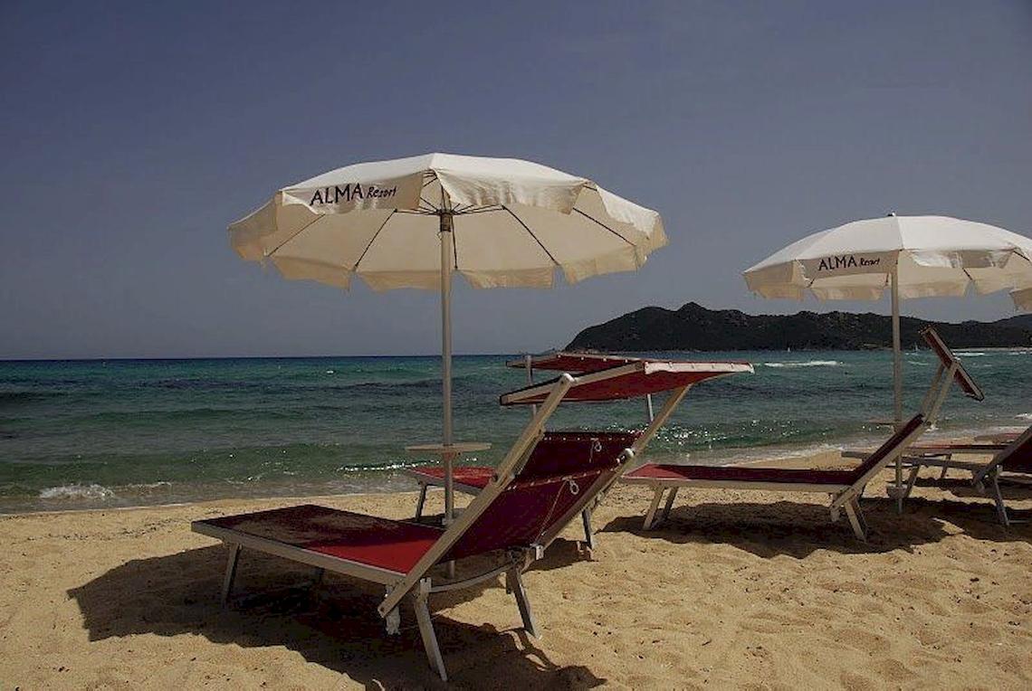 Strand mit roten Sonnenliegen und weißen Alma Resort Sonnenschirmen