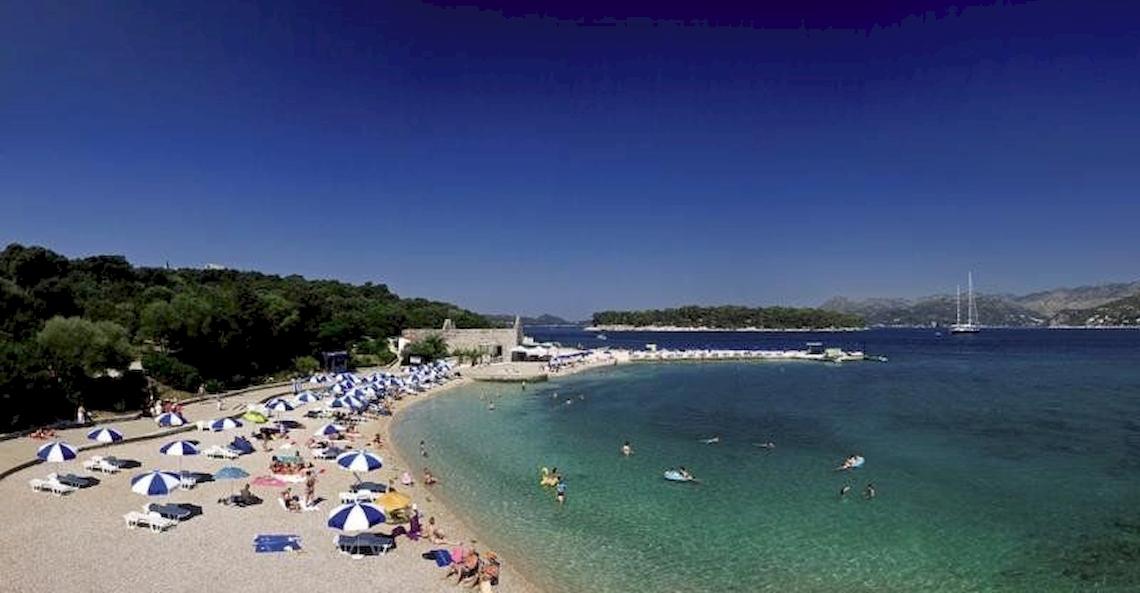 Valamar Tirena Hotel Strand mit vielen Sonnenschirmen und Gästen, die schwimmen und entspannen.
