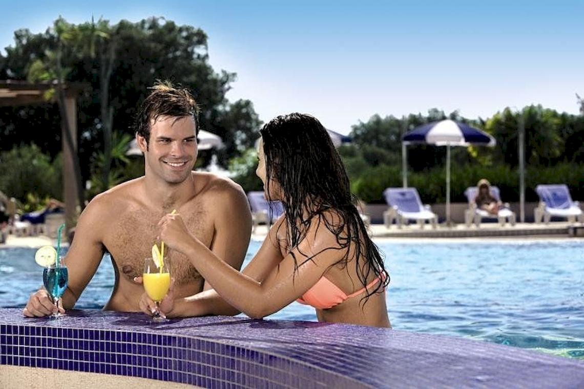 Mann und Frau sitzen am Poolrand im Valamar Tirena Hotel und trinken Cocktails.