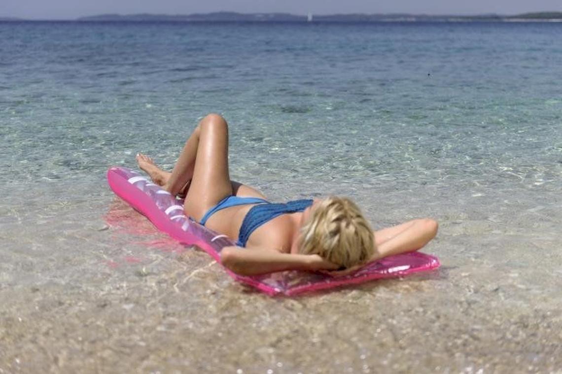 Frau liegt entspannt auf einer rosa aufblasbaren Matte im Wasser.