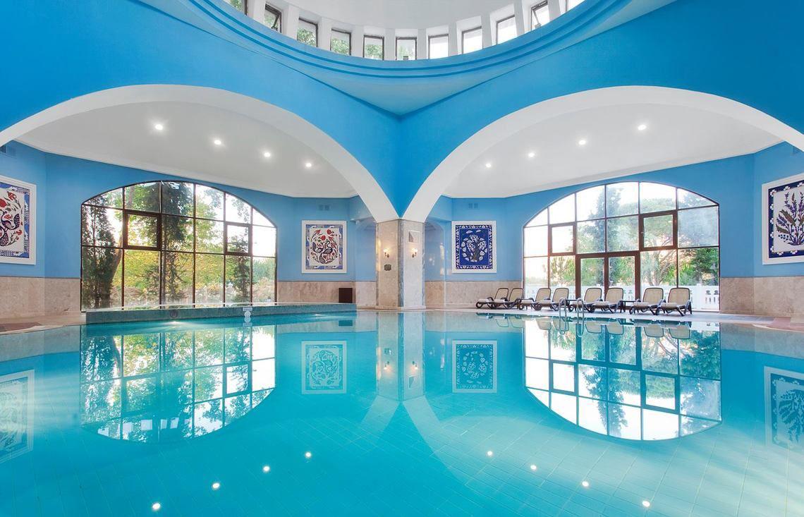 Ein blauer Swimmingpool im Swandor Hotels & Resorts Topkapi Palace mit Lounge-Stuhlreihen.