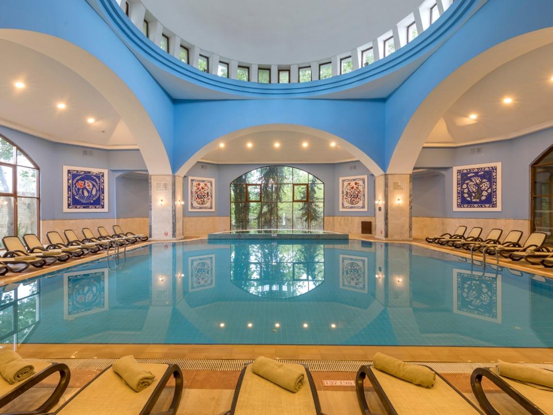 Innenansicht des Schwimmbads im Swandor Hotels & Resorts Topkapi Palace, mit blauen Wänden und Liegestühlen.