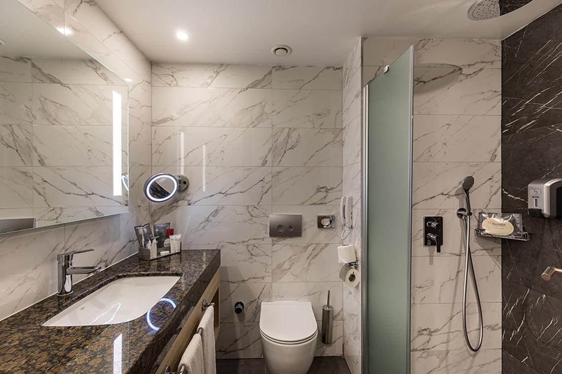 Badezimmer des Swandor Hotels & Resorts Topkapi Palace mit Marmorwänden und einer Glasdusche.