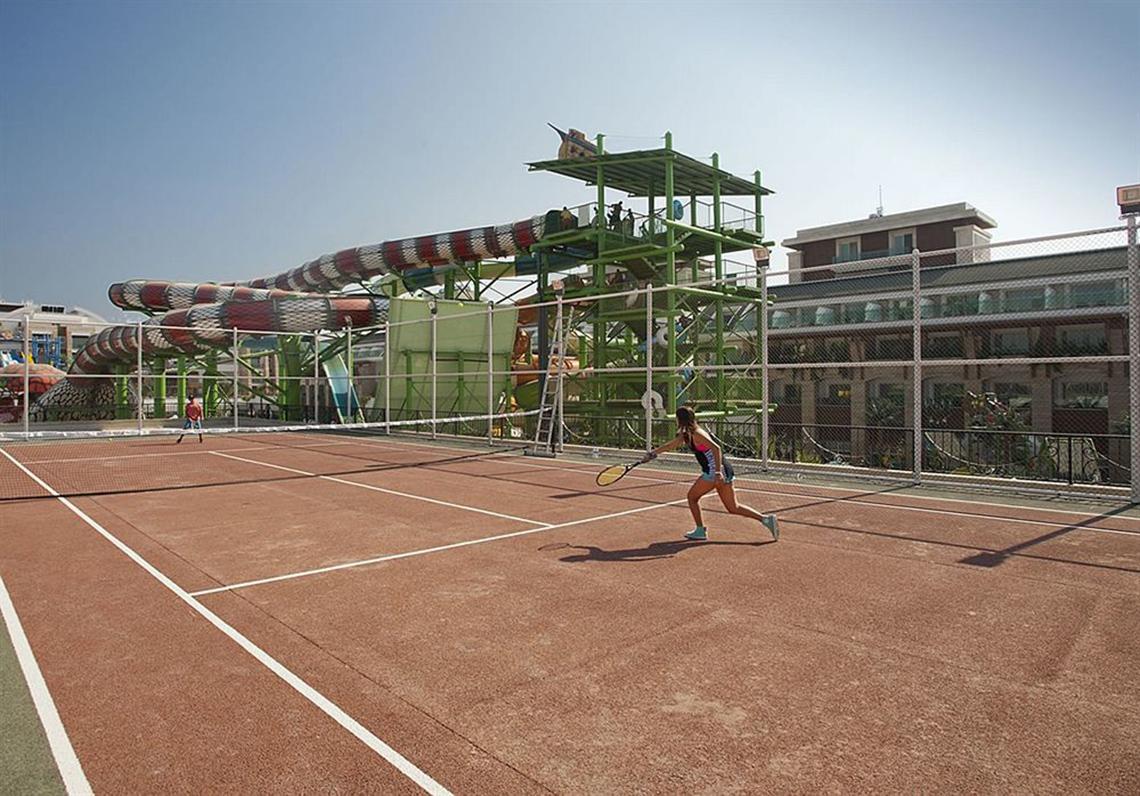 Tennisplatz im Crystal Waterworld Aqua Collection Hotel mit großer Wasserrutsche im Hintergrund.