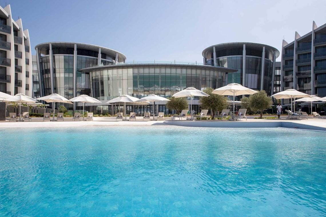 Ein Swimmingpool vor dem Jumeirah at Saadiyat Island Resort mit Sonnenschirmen und Liegestühlen.