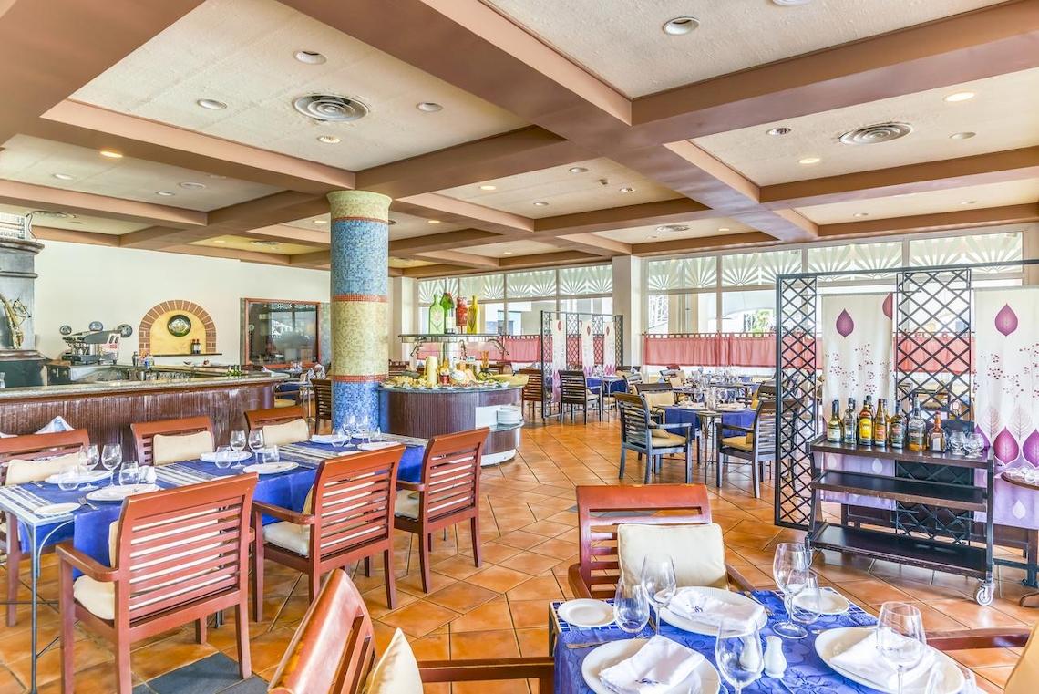 Innenansicht des Restaurants im Royalton Hicacos Resort & Spa mit blauen Tischdecken und Holzstühlen.