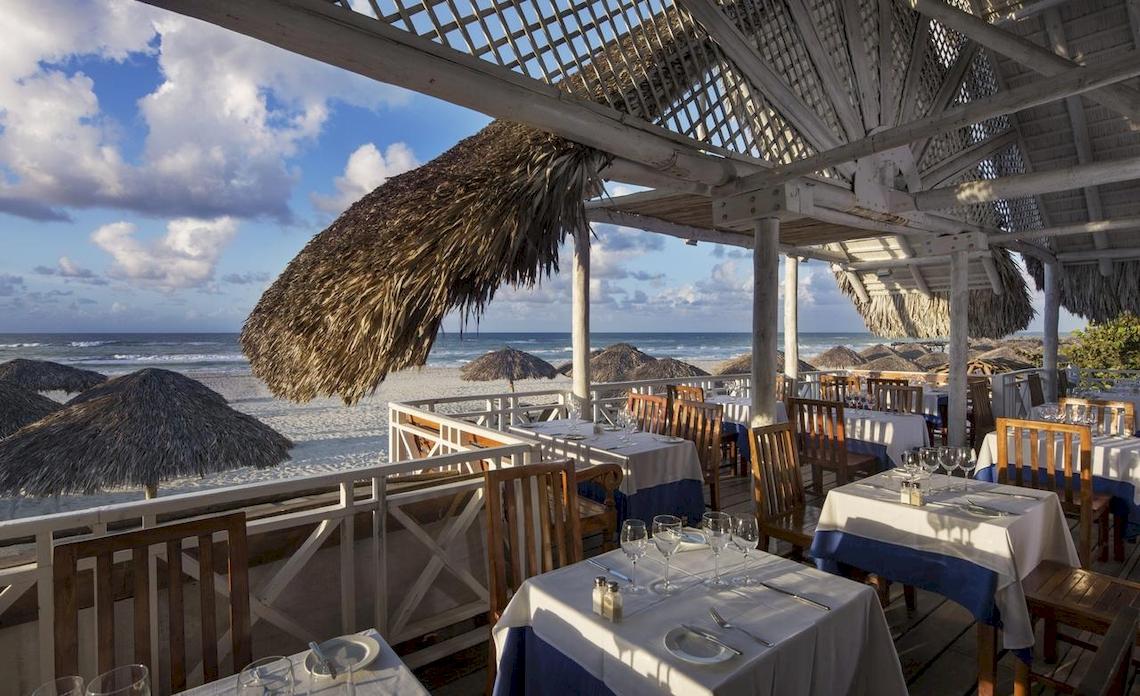 Außenterrasse des Royalton Hicacos Resort & Spa mit Tischen und Stühlen unter Strohdächern am Strand