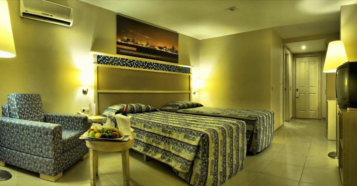 Doppelzimmer im Ephesia Holiday Beach Club mit zwei Betten, Tisch, Stuhl und Obstteller.