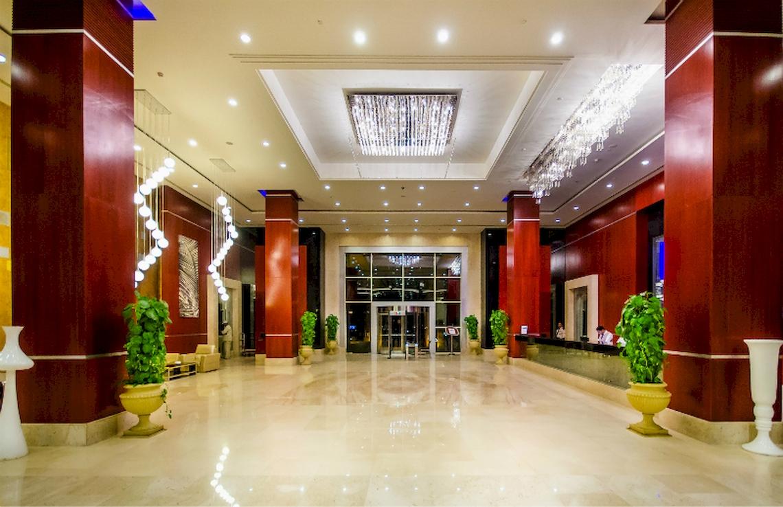 Empfangsbereich des Serenity Alma Heights Hotels mit luxuriöser Einrichtung und Pflanzen in gelben Vasen.