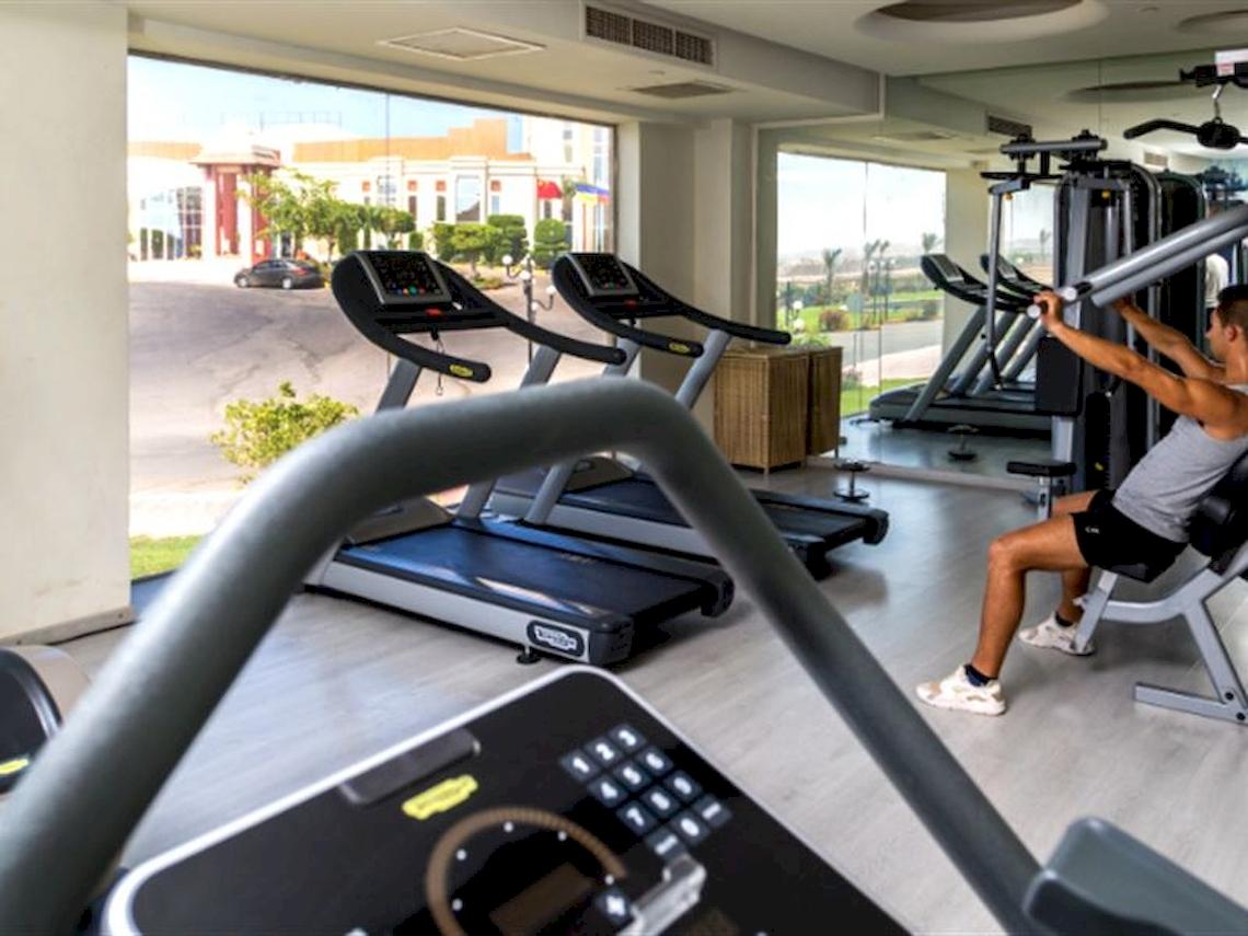 Fitness-Center im Serenity Alma Heights Hotel mit mehreren Laufbändern und einem Mann, der an einem Gerät trainiert.