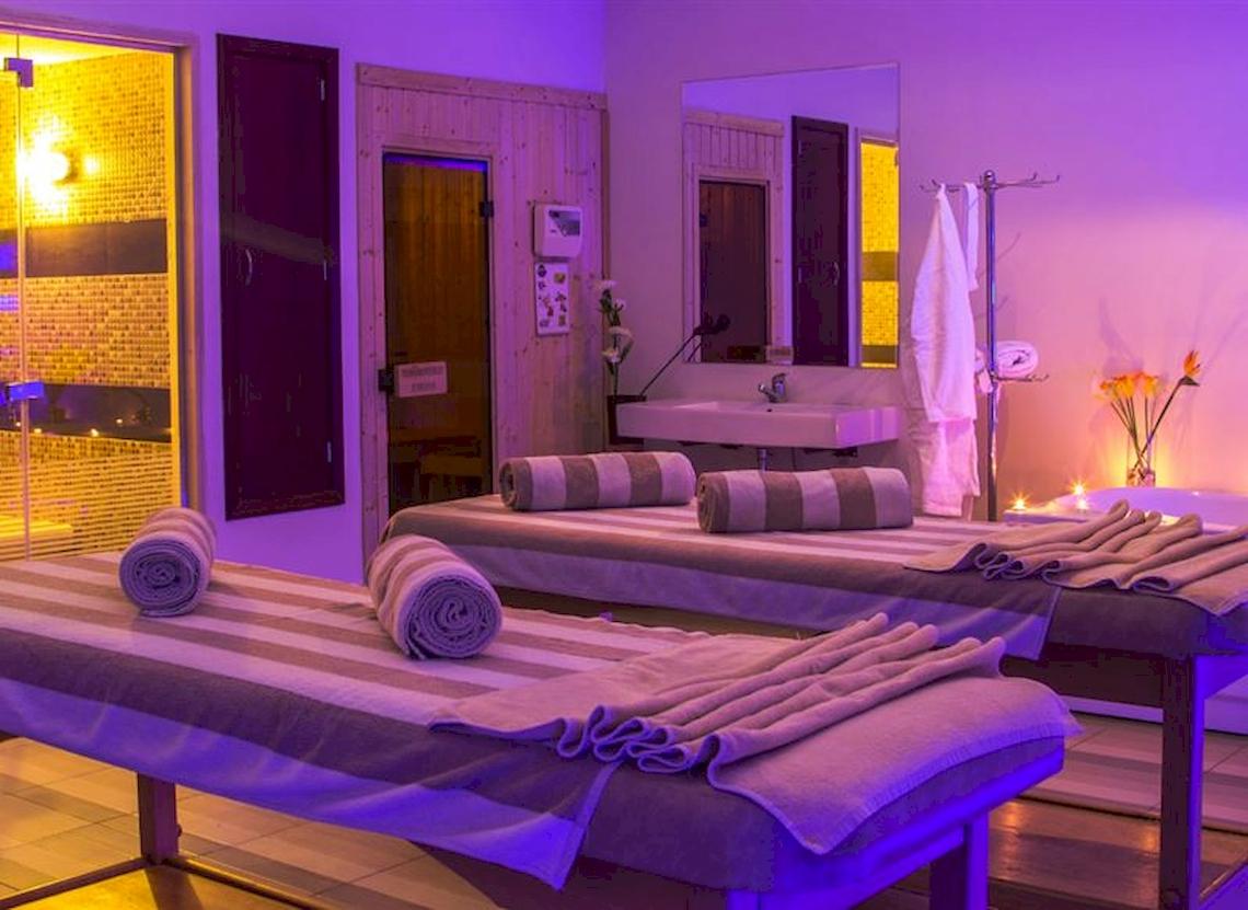 Behandlungsraum im Serenity Alma Heights Spa mit zwei Massageliegen, violetten Lichtern und einem Waschbecken.